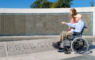 older man in a wheelchair and his grand daughter looking at the stars of the fallen at the world war ii memorial in washington, dc.