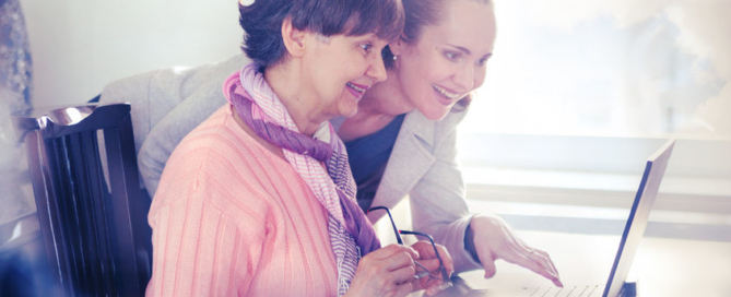 younger woman helping an elderly person using laptop computer for internet search. young and pension age generations working together.