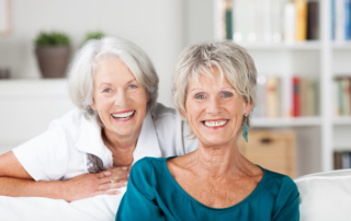 happy vivacious elderly female friends relaxing together in a living room and posing to smile at the camera