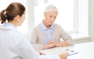medicine, age, health care and people concept - doctor with clipboard and senior woman meeting at hospital